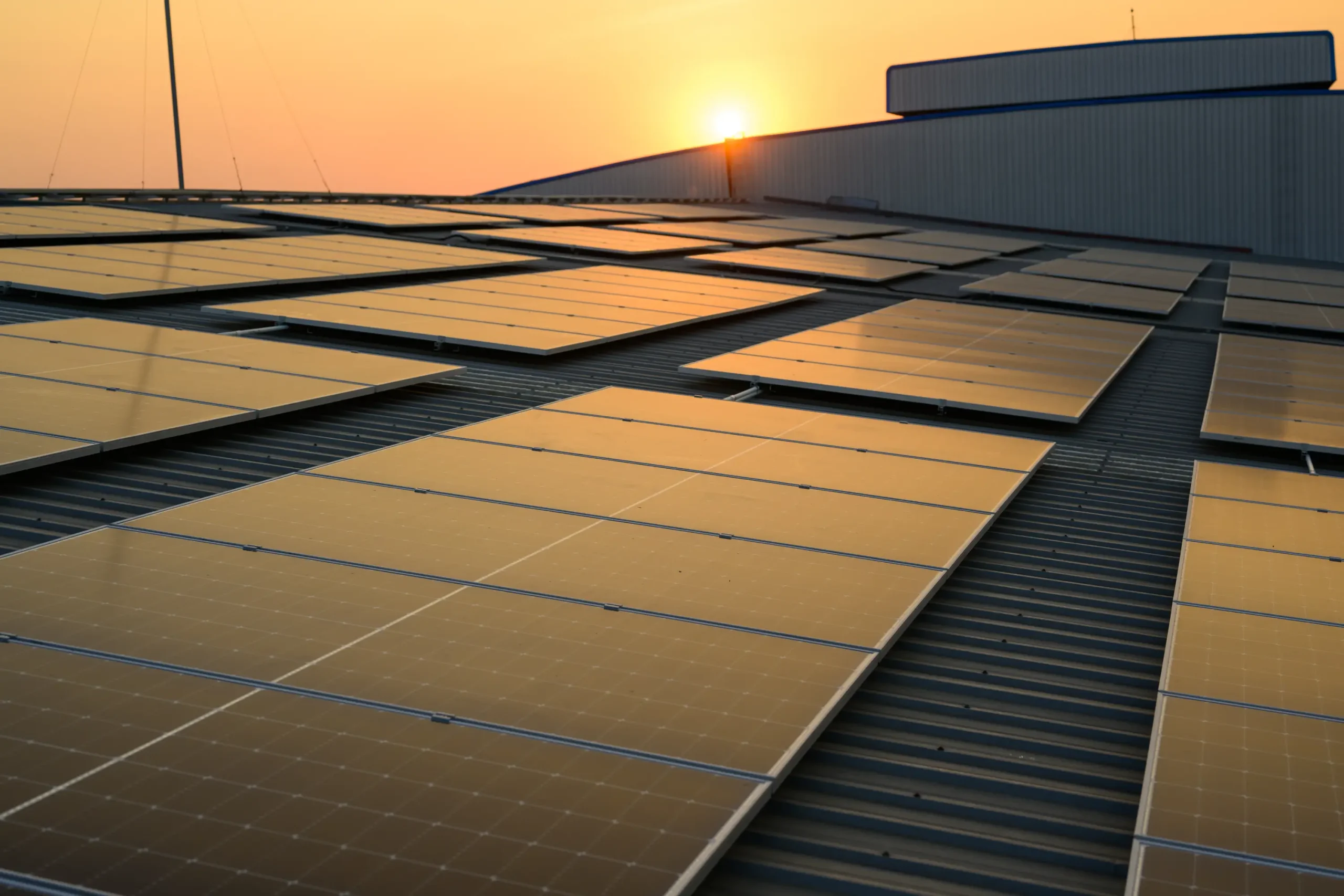 Rooftop solar panels beside an industrial building at sunset